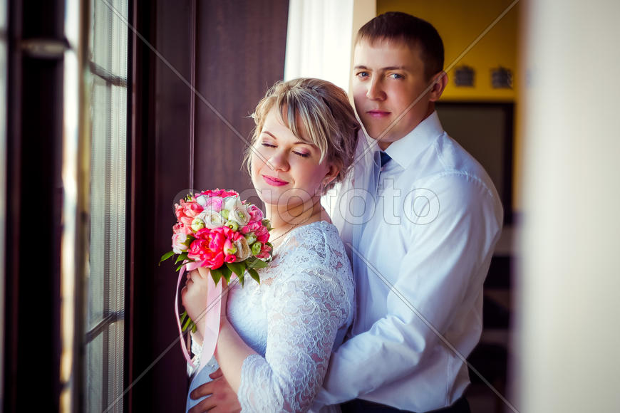 Невеста и жених стоят у окна в обнимку