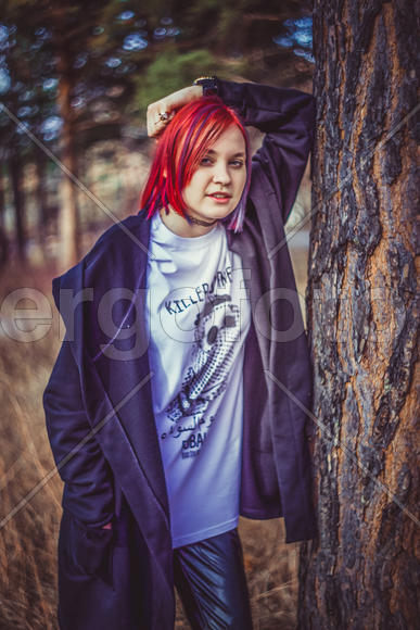Девушка с ярко-красными волосами стоит около дерева 