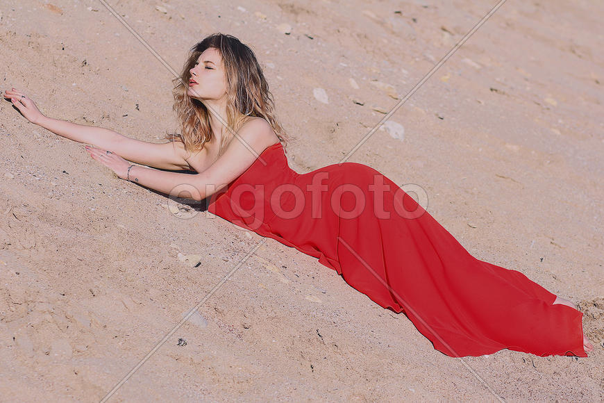 Девушка-блондинка в красном платье на песке
