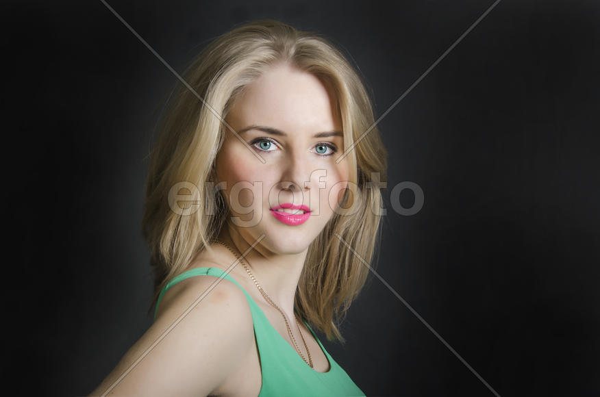 Beautiful blond girl with blue eyes in the green dress smiling on a dark background