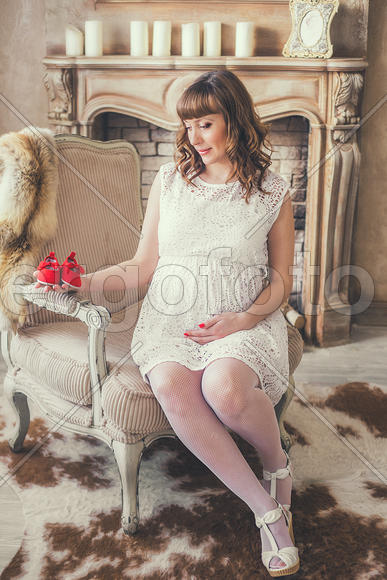 Беременная девушка в белом платье в кресле у камина