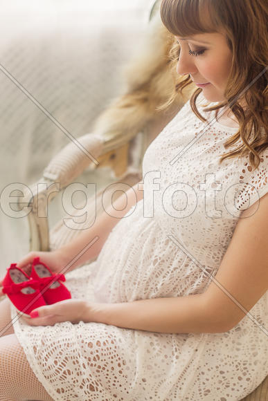 Беременная девушка в кресле держит детскую обувь