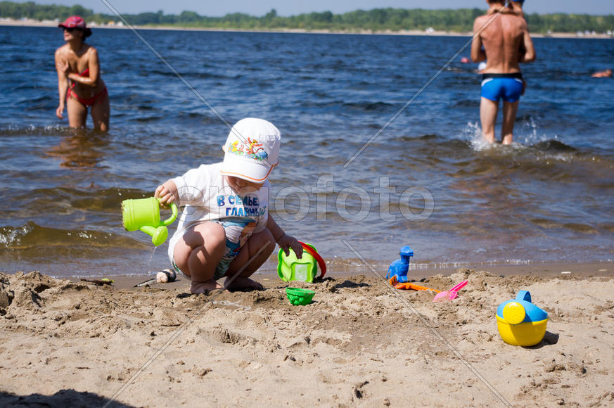 Мальчик играет с лейкой на берегу реки 
