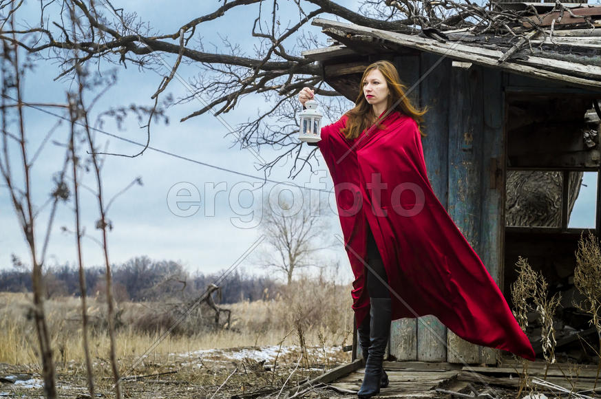 Девушка в красном плаще, с фонарём в руках, на пороге лесной хижины