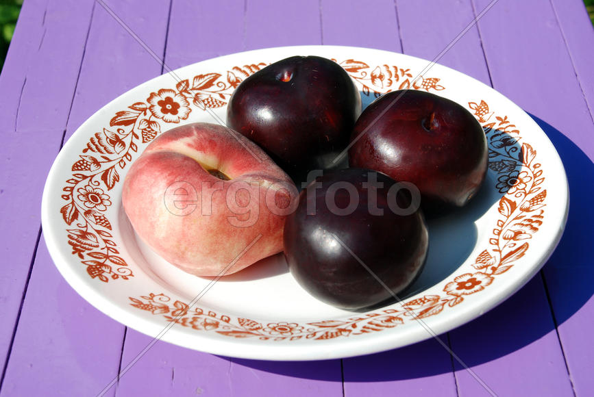 Один персик и три сливы на тарелке с узорами
