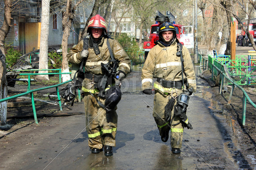 Пара пожарных идет по улице после тушения пожара