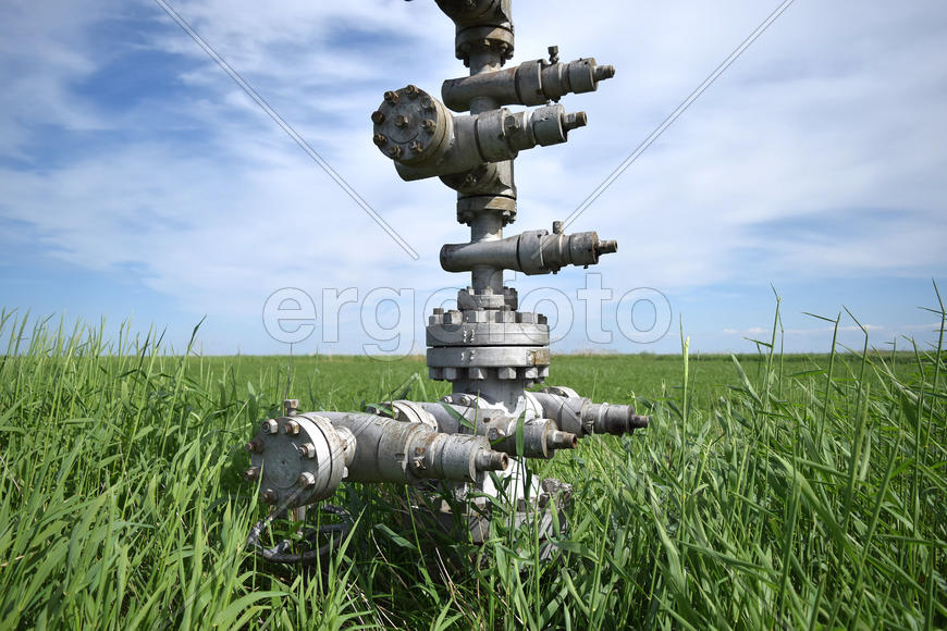 Canned oil well against the sky and field. Equipment of an oil well. Shutoff valves and service