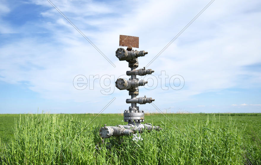 Canned oil well against the sky and field. Equipment of an oil well. Shutoff valves and service