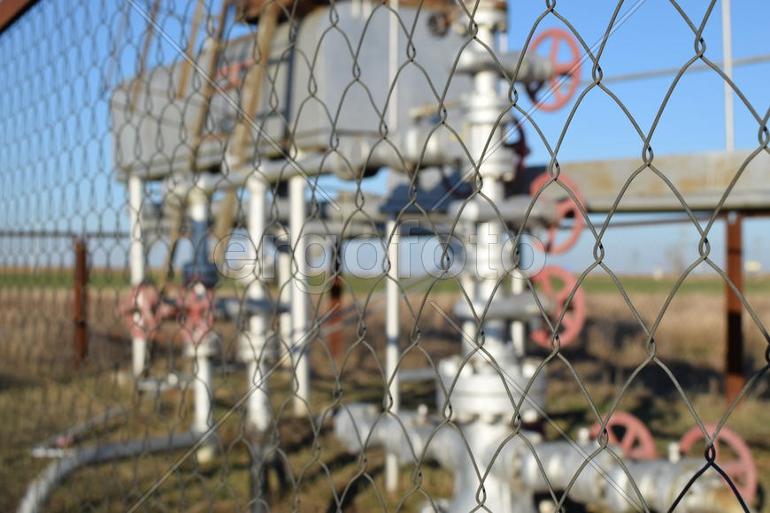 Grid the chain-link near an oil well. Shutoff valves and service equipment