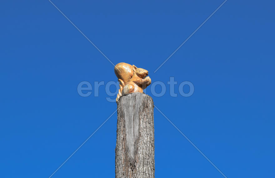 Фигурка белочки с орехом на пне дерева на фоне голубого 