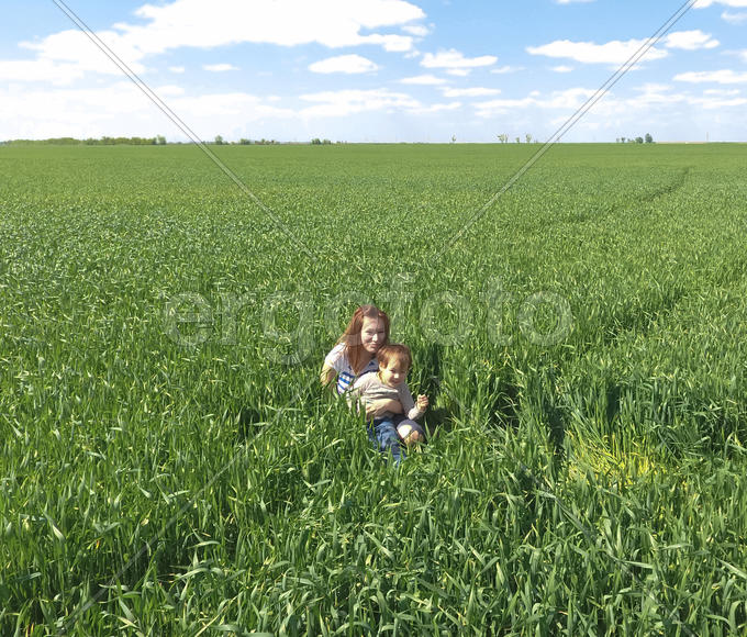 Молодая девушка с ребенком сидит в траве на поле.