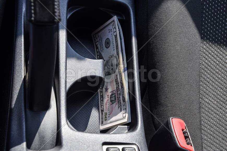 Несколько купюр американских долларов лежат в нише центральной консоли автомобиля