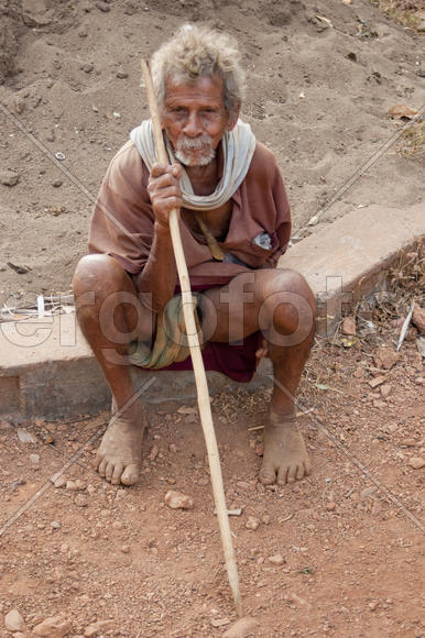 Rustic old man sitting on the ground with a stick in his hands