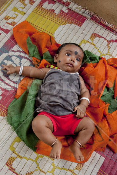 Indian baby lying on colorful mat in the village