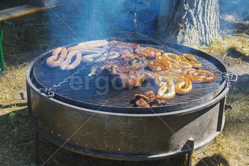 Roast large chunks of meat and sausage on a large grill