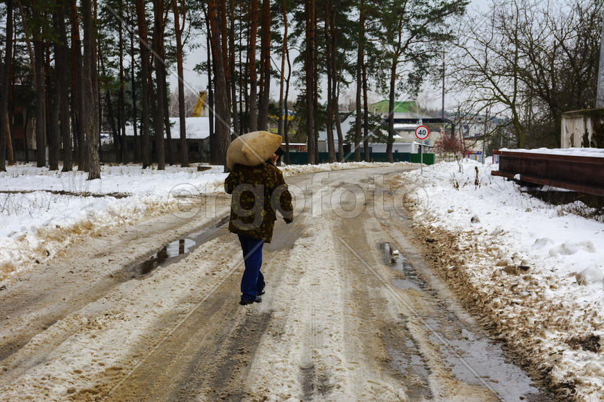 Человек несет большой мешок по дороге покрытой снегом 