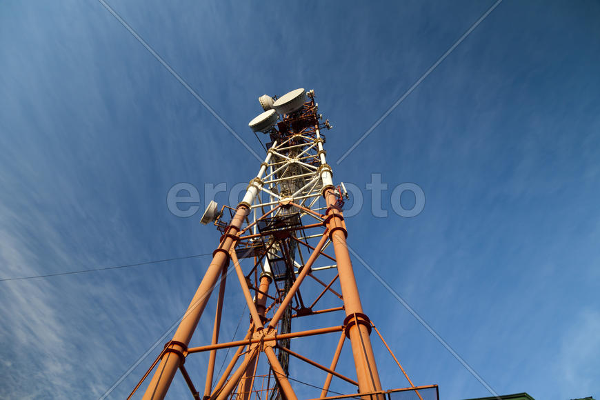 Communication tower against the bright blue sky with clouds