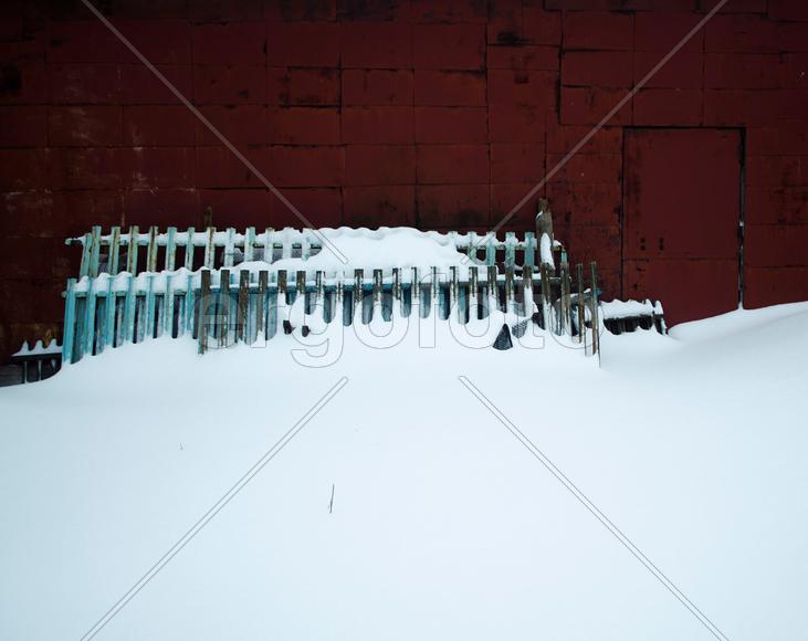 Забор в снегу у красной стены 