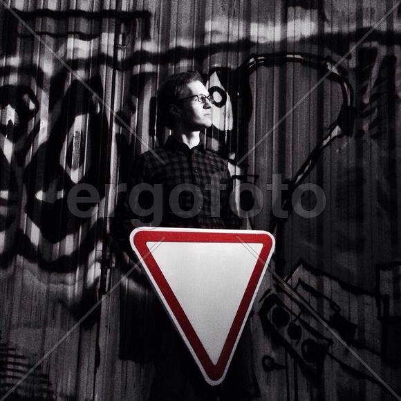 Молодой человек держит дорожный знак на фоне граффити стены