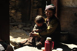 Тибетская женщина в Непале с ребенком угощает чаем на улице сидя на полу  у входа в храм