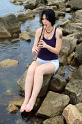 Девушка с татуировкой играет на японской медитативной флейте сякухати, сидя на камнях