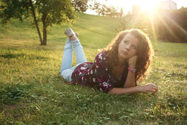 Девушка с длинными волосами в джинсах лежит на траве