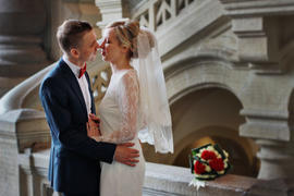 Жених и невеста обнимаются, сзади них них лежит миниатюрный букет невесты из красных и белых цветов 