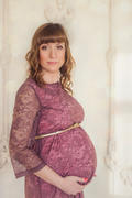 Беременная девушка в платье с поясом на фоне стены