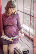 Беременная девушка читает книгу на окне