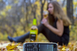 Телефон с СМС "прости" на фоне девуки пьющей вино и осеннего леса
