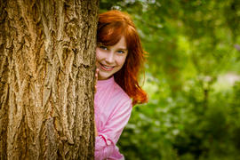 Девушка выглядывает из-за дерева