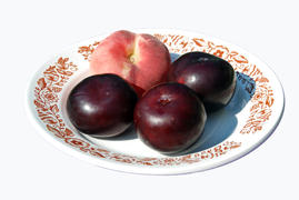 Один персик и три сливы лежат на белой тарелке с узорами