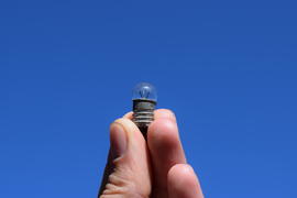 Bulb on 3 volts in a hand against the sky. Rarely used lamp