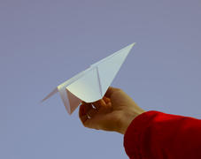 Бумажный самолётик в руке на фоне неба