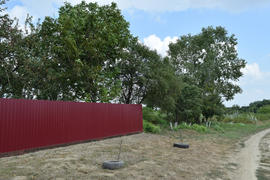Red fence of metal sheets on a background of green trees. Fence in the country