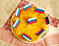 Russian pie cut into eight pieces lying on a platter with patriotic flags