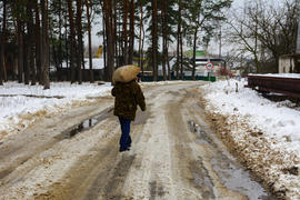 Человек несет большой мешок по дороге покрытой снегом 