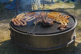 Roast large chunks of meat and sausage on a large grill