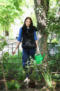 Positive casual dressed woman in yard gardening with watering can