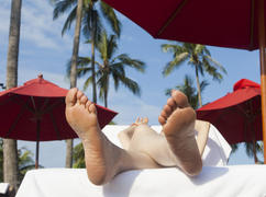 The person on vacation lies on a chaise lounge under an umbrella in beams of the tropical sun