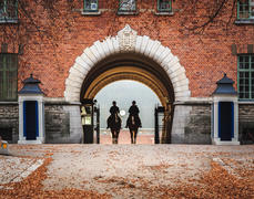 Двое всадников на лошадях верхом в арке кирпичного дома